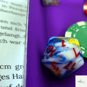 Ein Würfel liegt auf einer violetten Würfelunterlage und zeigt eine 1. Rechts neben dem Würfel liegt ein Pokerchip. Links vom Würfel sind Auszüge eines Textes zu sehen. Das alles war während des Abenteuer "Angriff der Killerfasane" für MIDGARD - Legenden von Damatu.